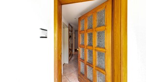 Un couloir avec une porte en bois dotée de panneaux de verre, un sol carrelé et un panneau indicateur fixé au mur.