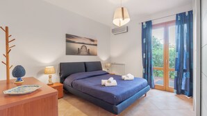 Une chambre à coucher avec un lit, une table de chevet en bois, une lampe, un tableau et une vue par la fenêtre.