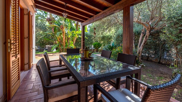 Une terrasse extérieure avec une table en verre et des chaises en osier, entourée d’une végétation luxuriante et agrémentée d’une pergola en bois.