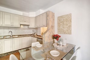 A modern kitchen with white cabinets, a marble island, and a dining area with glass tables and chairs.