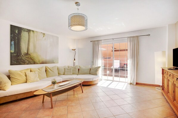 A living room with a sofa, a coffee table, a painting, a lamp, and a television.