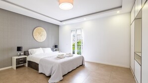 Une chambre moderne avec un lit, des tables de chevet, une lampe fixée au mur et une fenêtre donnant sur un beau paysage.
