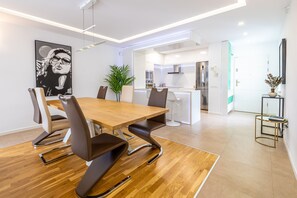 Un espace repas moderne avec une table et des chaises en bois, une cuisine en arrière-plan et une plante en pot.