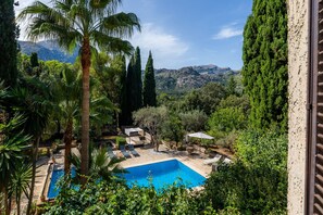 Une piscine entourée de palmiers et de cyprès, avec une vue sur les montagnes en arrière-plan.