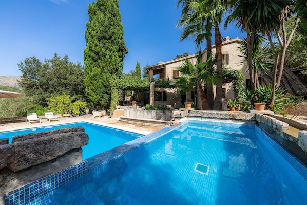 A swimming pool with a stone edge, a large tree, and a building with a balcony.