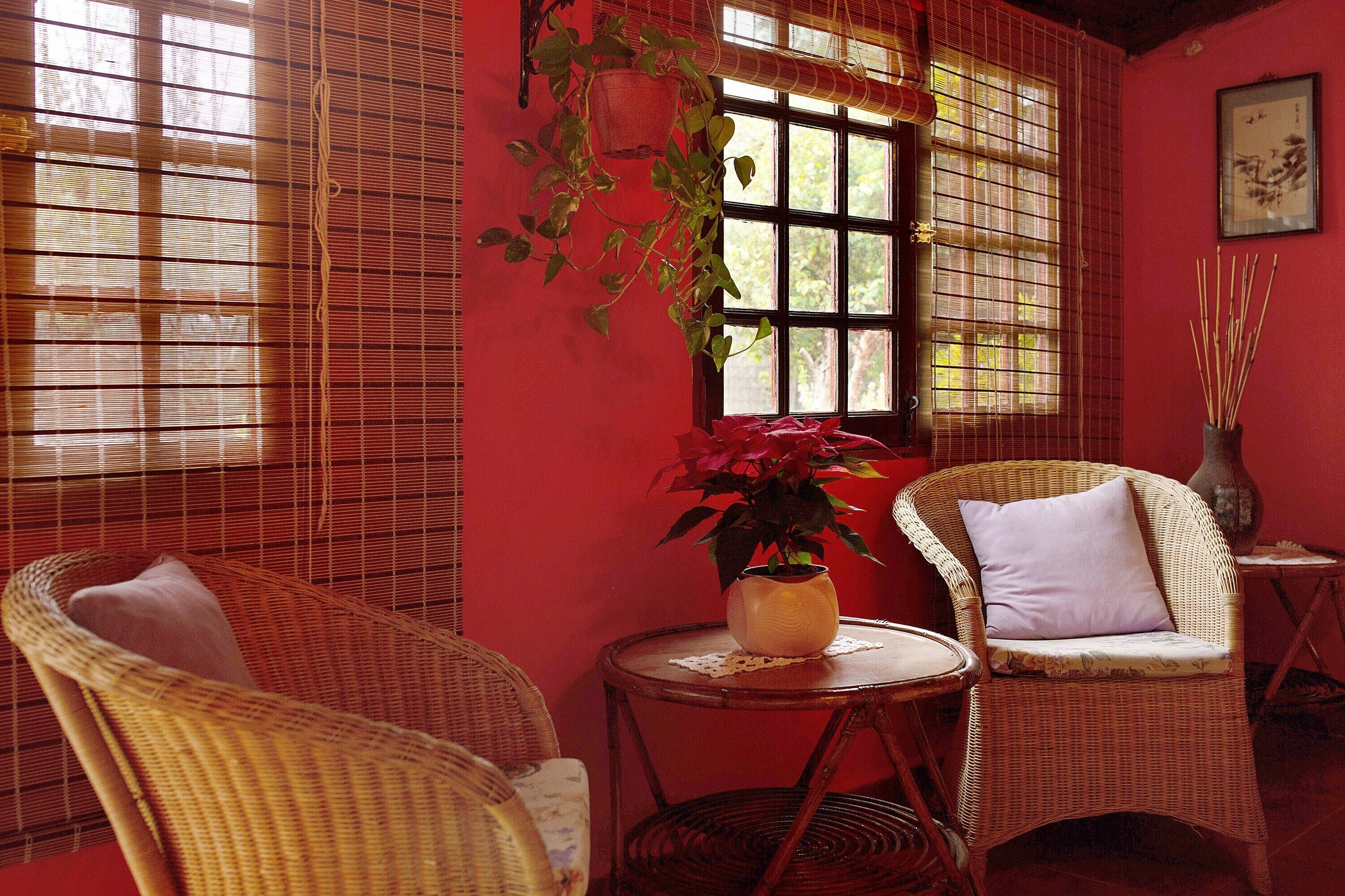 Una habitación con muebles de mimbre, una pared roja y una ventana con vistas.