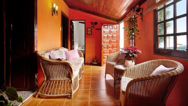 Una habitació amb sostre de fusta, un sofà de vímet, una taula de vímet i una finestra amb vistes.