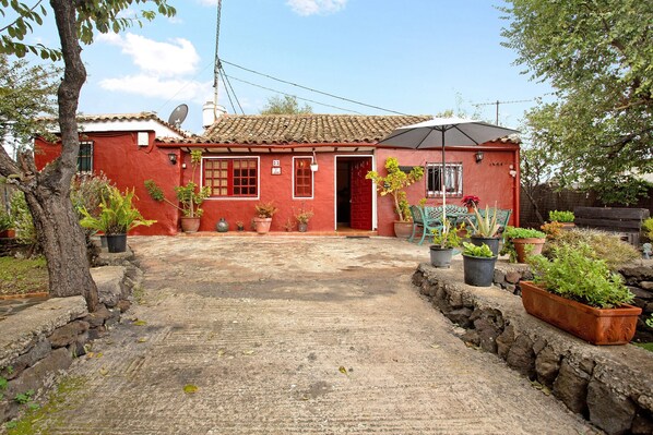 A red house with a tiled roof, a satellite dish, and potted plants.