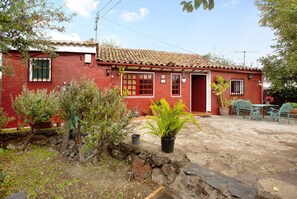 A red house with a tiled roof, a stone wall, and potted plants.
