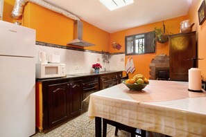 A kitchen with a white refrigerator, microwave, and stove, a wooden cabinet, and a table with a fruit bowl.