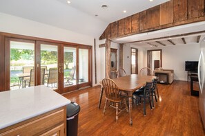 A spacious dining area with a large wooden table, chairs, and a view of the outdoors through sliding glass doors.