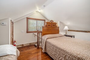 Un dormitorio con techo inclinado, cama de madera, mesita de noche, ventana con persianas, extintor de incendios y termostato en la pared.