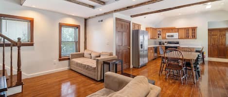 A spacious living area with a wooden floor, a sofa, a dining table with chairs, and a kitchen with wooden cabinets and appliances.