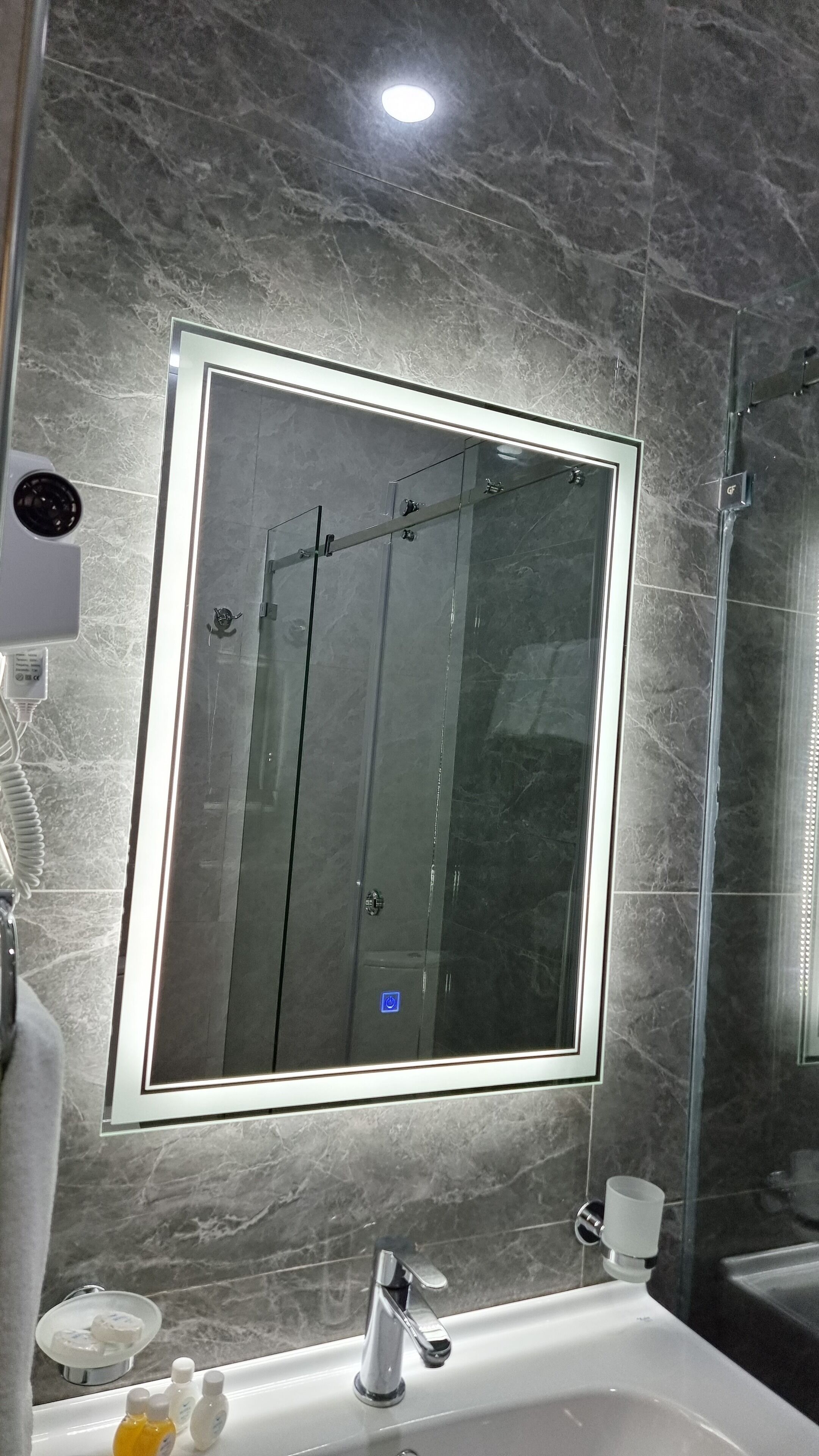 Une salle de bain dotée d’un grand miroir, d’une cabine de douche et d’un lavabo avec des articles de toilette.