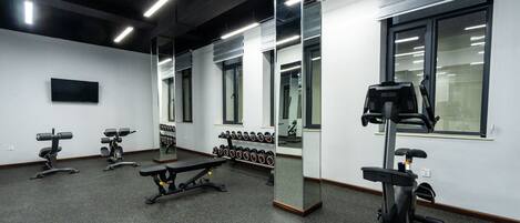 A gym with exercise equipment, a wall-mounted TV, and a mirror.