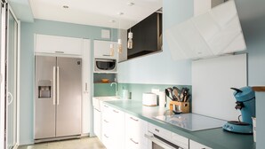 A modern kitchen with a stainless steel refrigerator, a microwave, a coffee maker, and a glass-top dining table.