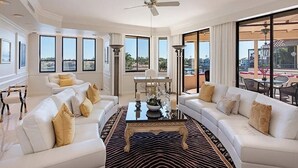 A spacious living room with white sofas, a central coffee table, and large windows offering views of the city. - Ardissone Penthouse at Venetian Village (Naples)