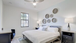 A bedroom with a bed, nightstands, a desk, a ceiling fan, and decorative wall art. - First Floor Corner Unit Condo On a Coveted Quad in Paseo of Fort Myers (Fort Myers)