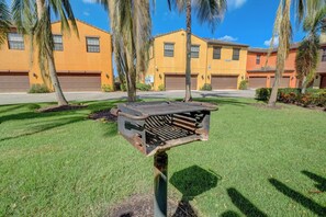 Um edifício residencial com várias garagens, um gramado bem cuidado e palmeiras.