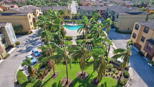 A residential area with a swimming pool surrounded by palm trees and a well-maintained lawn. - First Floor Corner Unit Condo On a Coveted Quad in Paseo of Fort Myers (Fort Myers)