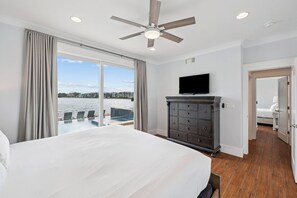 A bedroom with a large bed, a ceiling fan, a TV, and a view of the water.