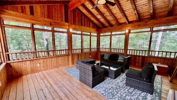Une terrasse en bois dotée d’un ventilateur de plafond, de grandes fenêtres et de mobilier d’extérieur.