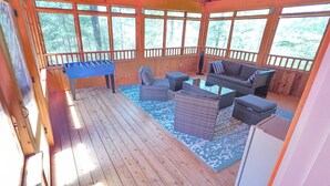 Une terrasse en bois avec une table de baby-foot, des meubles en osier et une vue sur la forêt.