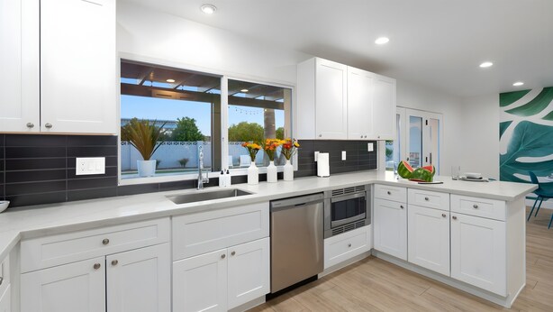 Una cocina moderna con armarios blancos, lavavajillas de acero inoxidable y un amplio ventanal con vistas al verdor.