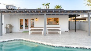 A covered patio with a pool, outdoor seating, and a grill.