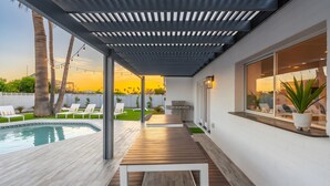 Un patio cubierto con piscina, sillas de descanso y una parrilla.