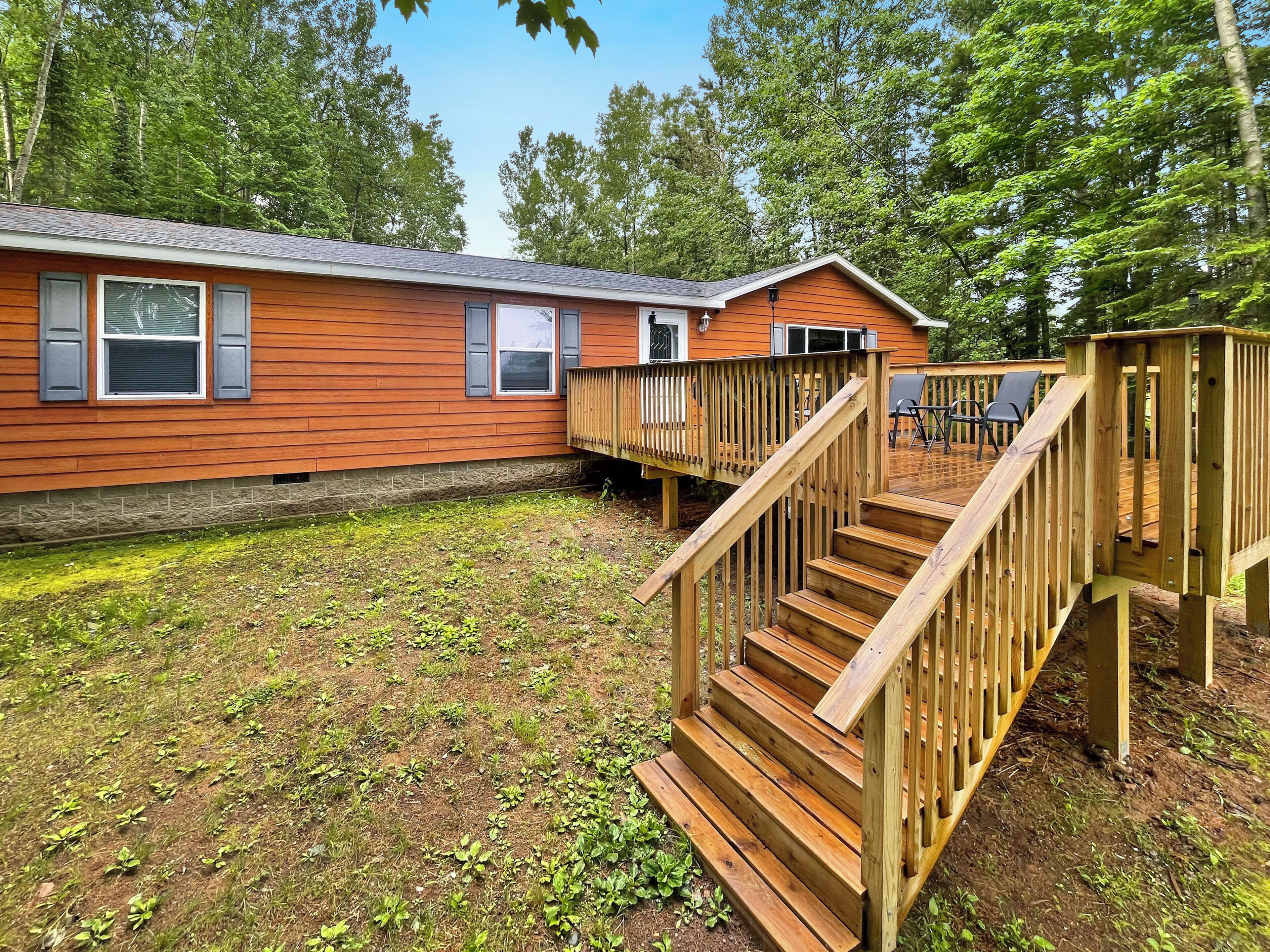 A wooden cabin with a deck and stairs, surrounded by trees.