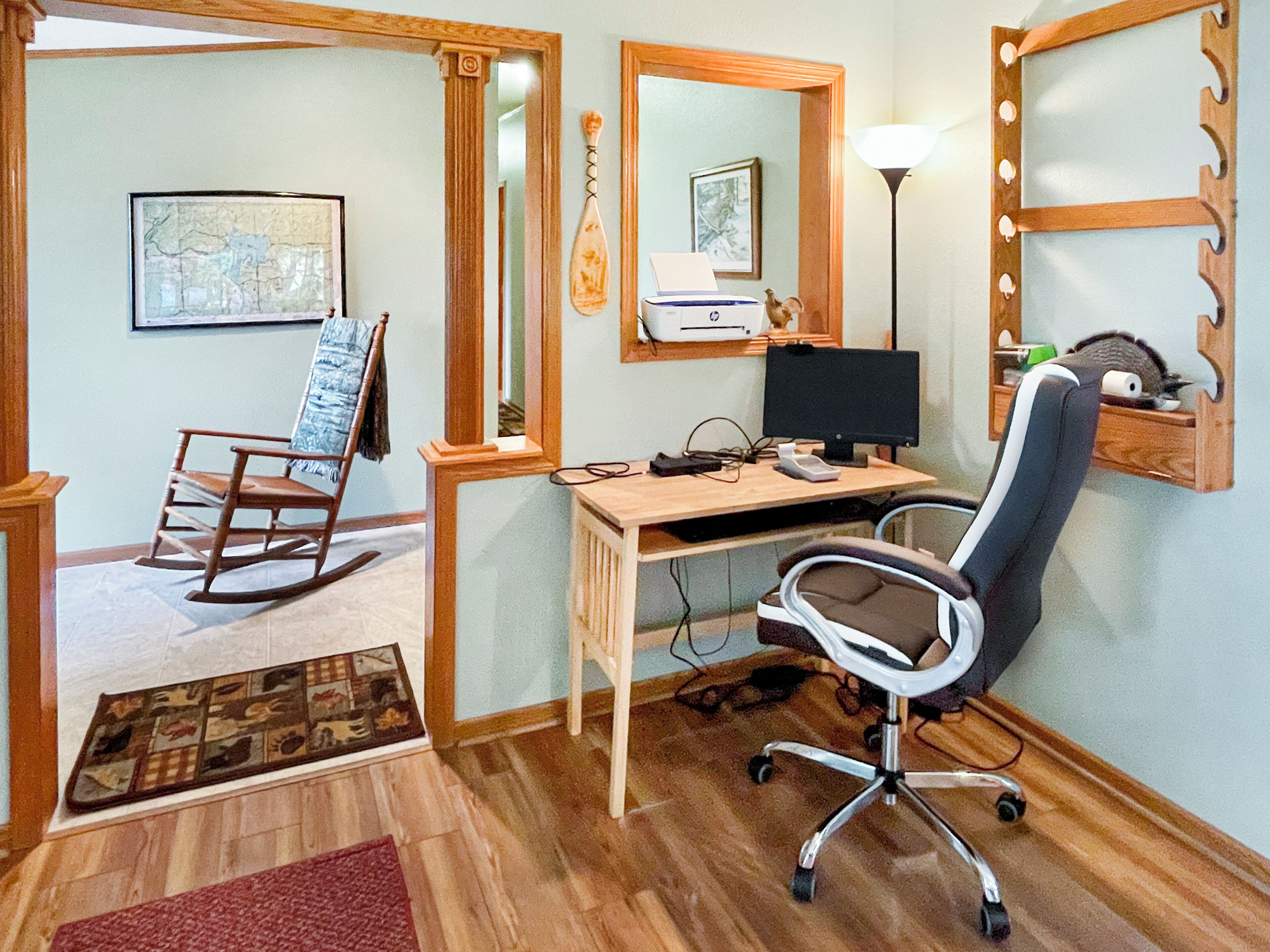 A room with a wooden desk, a rocking chair, a computer setup, and a mirror with lights.