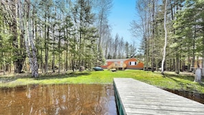 A wooden dock leading to a house surrounded by trees.