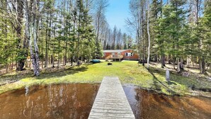 A wooden dock leading to a house surrounded by trees.