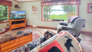 A living room with a television, a sofa, a coffee table, and a window with a view of a lake.