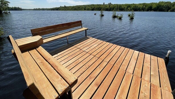 Un muelle de madera que se adentra en un lago tranquilo, con un banco y un pequeño motor fueraborda.
