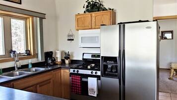 A kitchen with wooden cabinets, a stainless steel refrigerator, a microwave, a stove, and a sink.