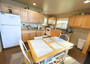 A kitchen with wooden cabinets, a white refrigerator, a dining table with chairs, and a window.