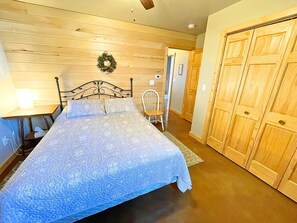 A bedroom with a bed, a chair, a wooden wardrobe, and a wall-mounted light fixture.