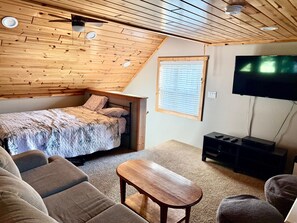 A bedroom with a sloped ceiling, a bed, a TV, and a seating area with a table.