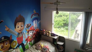 Un dormitorio infantil con un mural grande en la pared, una litera, una ventana con vistas y un ventilador de techo.