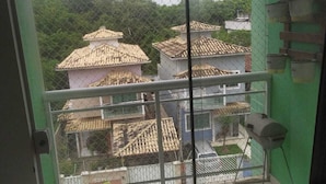 Un balcón con vistas a edificios residenciales, un muro verde y una parrilla para barbacoa.