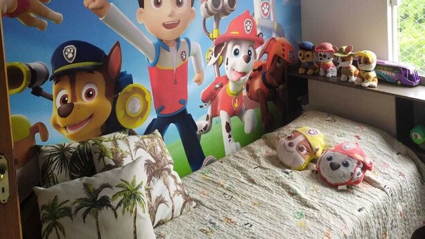 Un dormitorio con un gran mural en la pared de personajes animados, una cama con colcha estampada y una ventana con vistas a la vegetación.