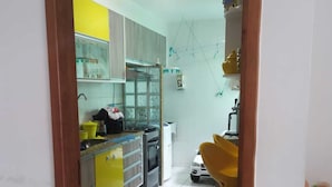 Una cocina con gabinetes amarillos, un refrigerador blanco y un lavamanos. Se ve una silla amarilla y un modelo de coche blanco al fondo.
