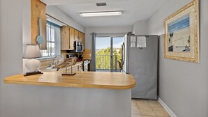 Cocina moderna con encimera de madera, microondas y refrigerador. Se ve vegetación a través de la ventana.