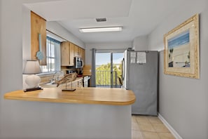 Cocina moderna con encimera de madera, microondas y refrigerador. Se ve vegetación a través de la ventana.