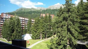 A balcony with a view of a mountain, trees, and a building with multiple floors. - Studio in Front De Neige Charvet Arc 1800 (Les Arcs)