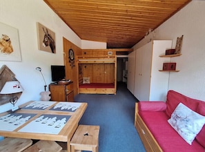 Una habitación acogedora con una cama litera, un sofá rojo, una mesa de madera con cartas y una lámpara.