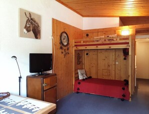 Une chambre avec un lit superposé, une télévision, une horloge et un mur orné d’un tableau.