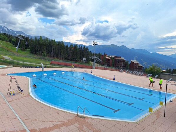 A swimming pool with lanes, a lifeguard, and a view of mountains.